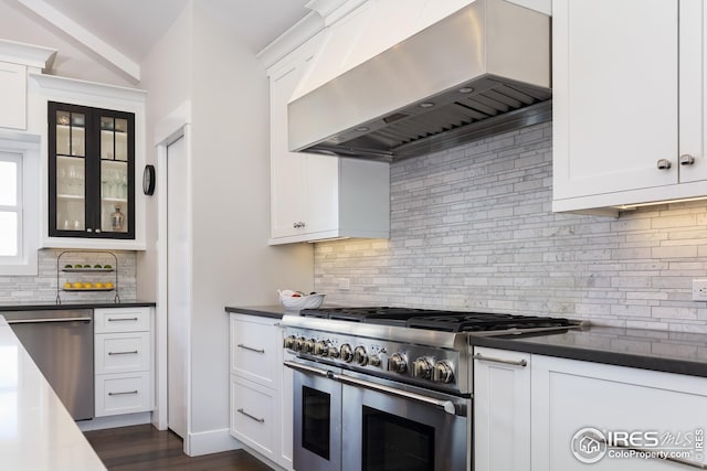 kitchen featuring dark countertops, tasteful backsplash, wall chimney range hood, and stainless steel appliances
