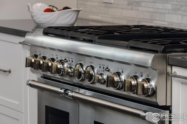details featuring high end range, white cabinetry, and decorative backsplash