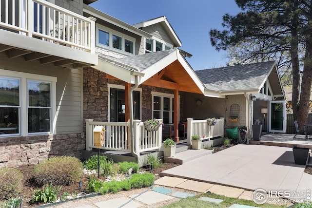 exterior space featuring a balcony, a shingled roof, a porch, and stone siding
