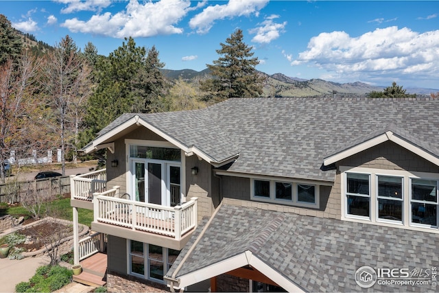 rear view of house with a shingled roof, a deck with mountain view, and stone siding