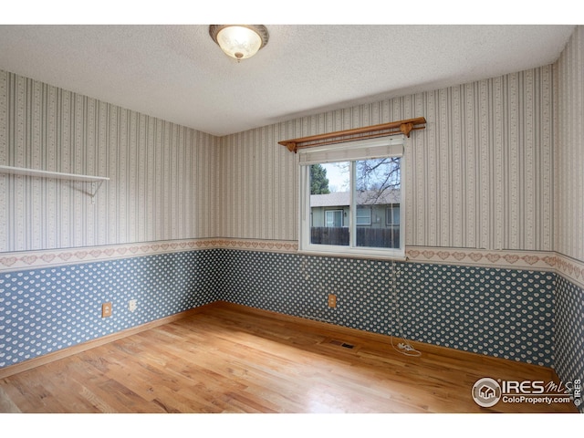 empty room featuring visible vents, wood finished floors, and wallpapered walls