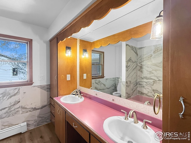 26237 County Road 65, Holyoke, CO 80734 - bathroom with baseboard heating, double vanity, wood finished floors, tile walls, and a wainscoted wall