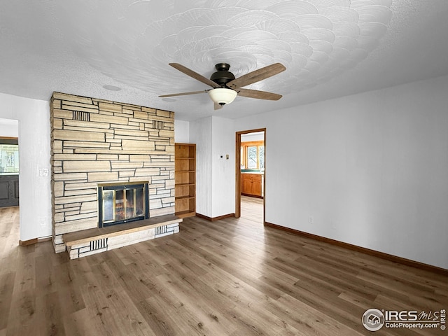 26237 County Road 65, Holyoke, CO 80734 - unfurnished living room featuring baseboards, wood finished floors, a fireplace, a ceiling fan, and a textured ceiling