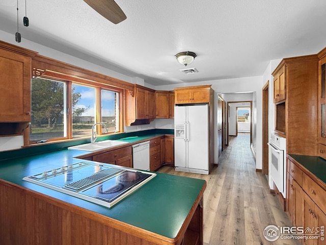 26237 County Road 65, Holyoke, CO 80734 - kitchen with white appliances, a sink, brown cabinetry, light wood finished floors, and a peninsula