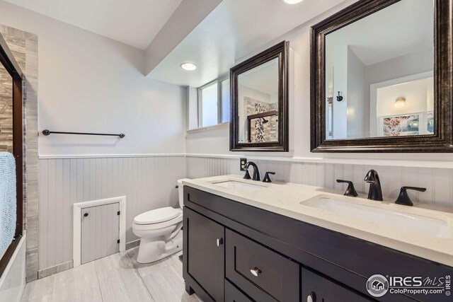 full bath with a sink, wainscoting, toilet, and double vanity