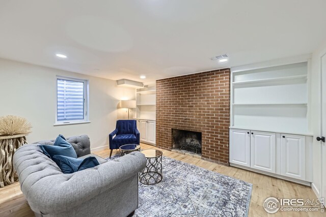 living room featuring a brick fireplace, built in features, recessed lighting, light wood-type flooring, and visible vents