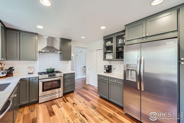 kitchen featuring light wood finished floors, light countertops, wall chimney exhaust hood, stainless steel appliances, and recessed lighting