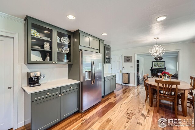 kitchen with stainless steel fridge, light countertops, an inviting chandelier, and glass insert cabinets