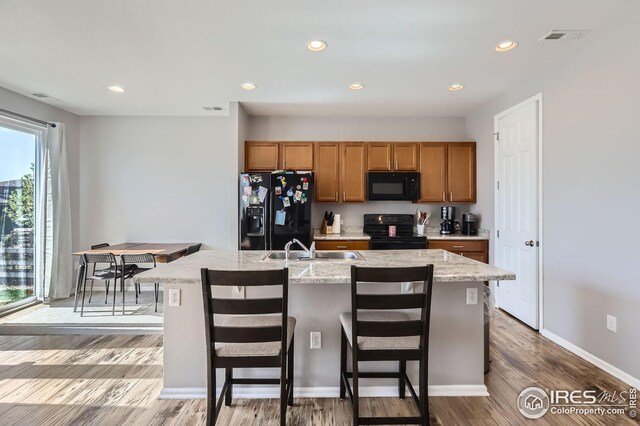 357 Chipman Dr, Windsor, CO 80550 - kitchen with a sink, a kitchen island with sink, brown cabinetry, visible vents, and black appliances