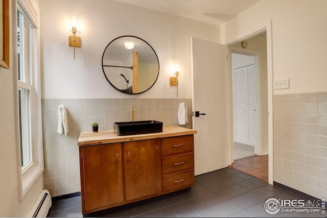 bathroom with tile walls, wainscoting, vanity, a baseboard radiator, and tile patterned floors