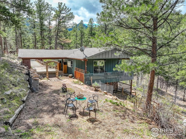 back of property with a shingled roof, board and batten siding, and a forest view