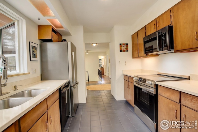 kitchen featuring dark tile patterned floors, light countertops, brown cabinets, a sink, and stainless steel appliances