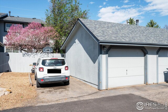 view of home's exterior featuring fence, a shingled roof, a garage, an outbuilding, and a chimney