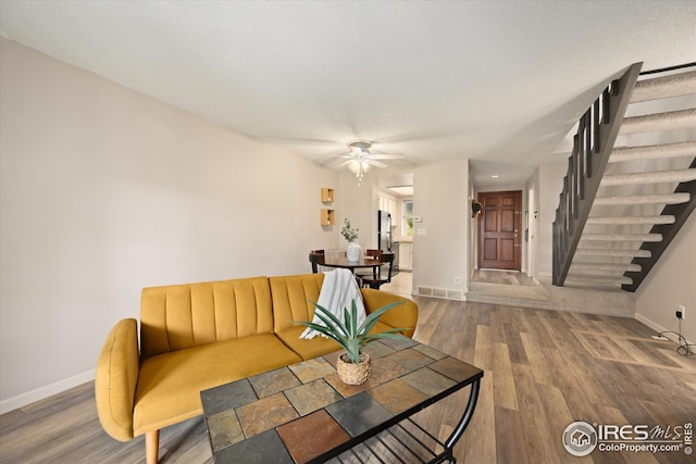 living area featuring visible vents, wood finished floors, baseboards, stairway, and a ceiling fan
