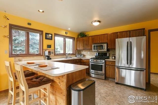7127 Coal Creek Canyon Hwy, Nederland, CO 80466 - kitchen with appliances with stainless steel finishes, a peninsula, light countertops, brown cabinets, and decorative backsplash