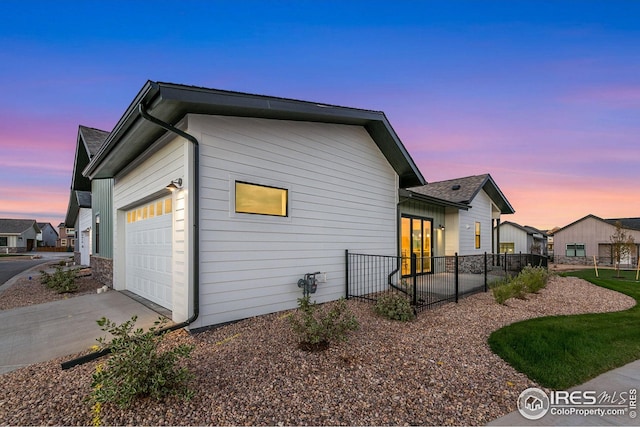 property exterior at dusk with concrete driveway, fence, and a garage