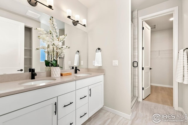 full bathroom featuring a sink, a walk in closet, double vanity, and a stall shower