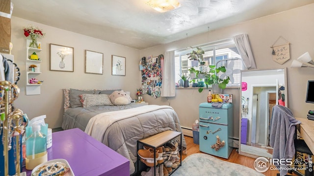 bedroom featuring wood finished floors and a baseboard heating unit