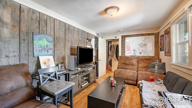 living room featuring stacked washing machine and dryer, light wood-type flooring, and wood walls