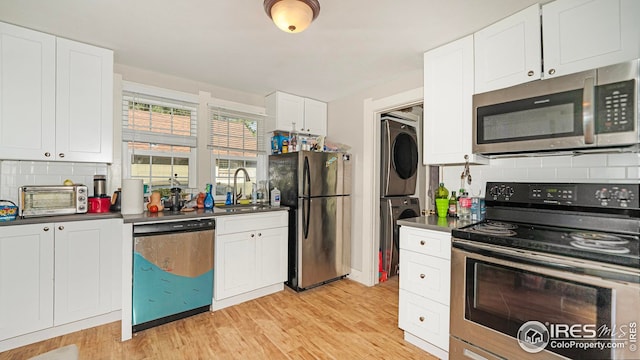 kitchen featuring stainless steel appliances, stacked washing machine and dryer, a sink, decorative backsplash, and white cabinetry