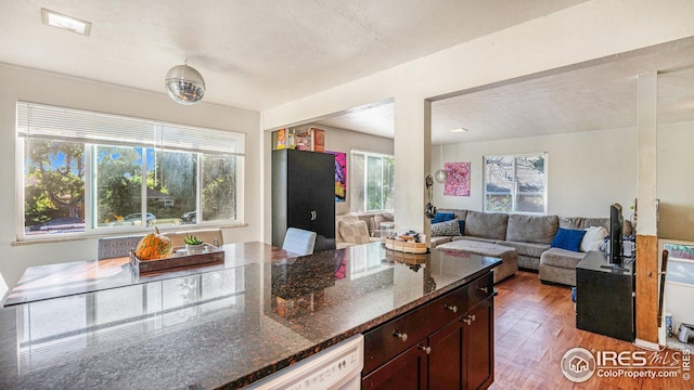 kitchen featuring light wood-type flooring, dark stone countertops, open floor plan, and dark brown cabinetry