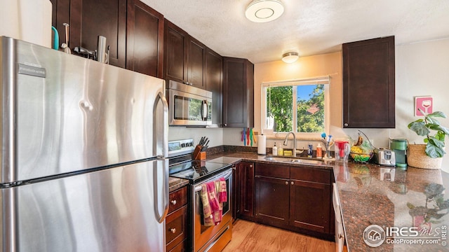 kitchen with stainless steel appliances, a sink, dark brown cabinets, light wood finished floors, and a textured ceiling