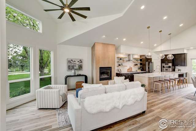 living area featuring high vaulted ceiling, a ceiling fan, a large fireplace, light wood-style flooring, and recessed lighting
