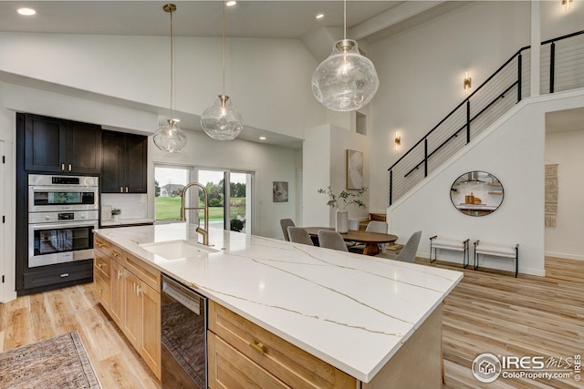 kitchen with a sink, high vaulted ceiling, dishwashing machine, stainless steel double oven, and light stone countertops