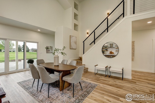 dining area with a towering ceiling, stairway, light wood-type flooring, baseboards, and recessed lighting