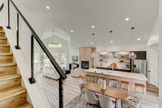 dining room featuring stairs, light wood-style flooring, a ceiling fan, recessed lighting, and high vaulted ceiling