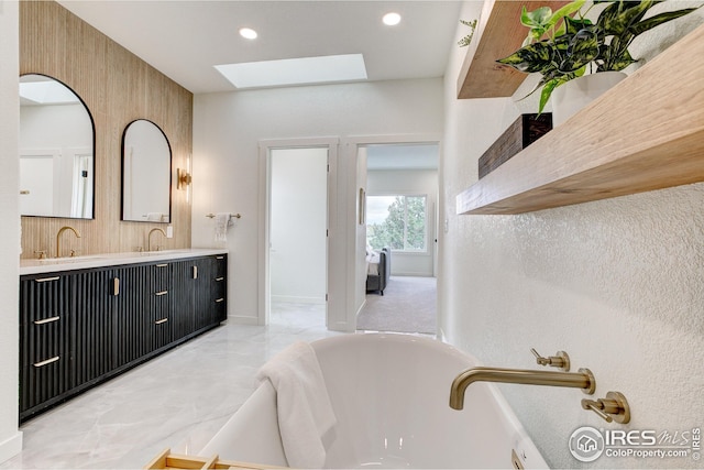 bathroom with a skylight, a freestanding bath, double vanity, marble look tile flooring, and recessed lighting