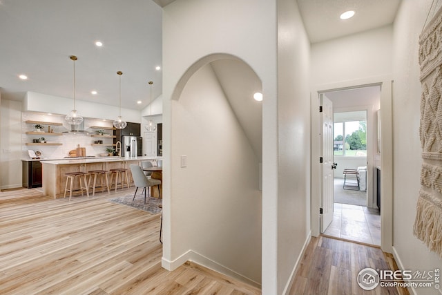 corridor featuring light wood finished floors, arched walkways, recessed lighting, and baseboards