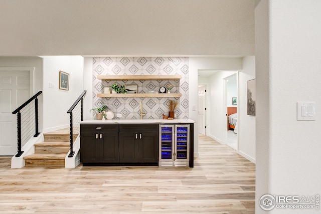 indoor dry bar with beverage cooler, light wood-style flooring, baseboards, and stairs