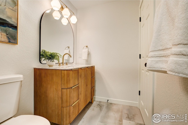 half bathroom with wood finished floors, toilet, vanity, and baseboards