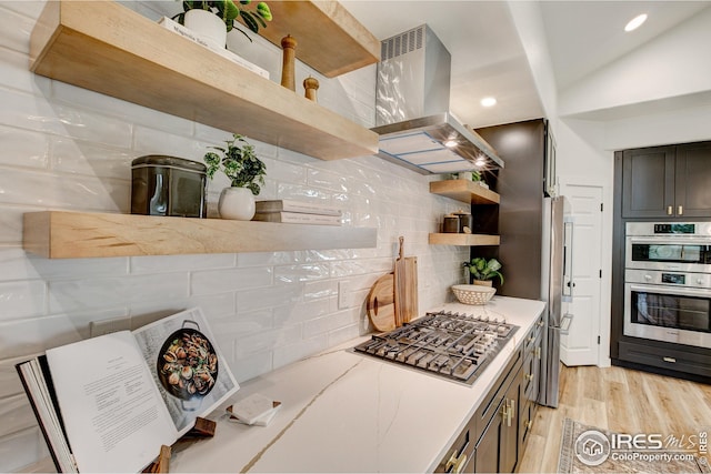 kitchen with open shelves, stainless steel appliances, island exhaust hood, decorative backsplash, and light wood-style flooring