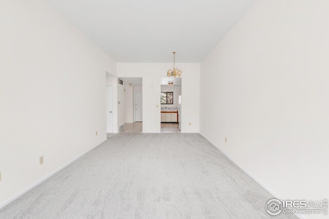 unfurnished room featuring light carpet and a chandelier
