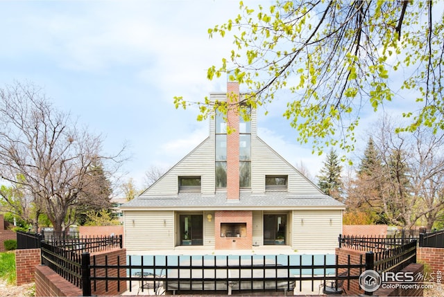 rear view of house with a patio, a fenced front yard, a chimney, and roof with shingles