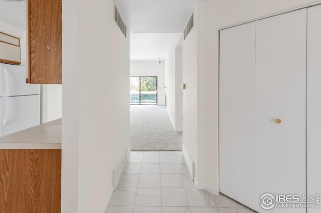 hallway featuring light colored carpet, light tile patterned floors, and baseboards