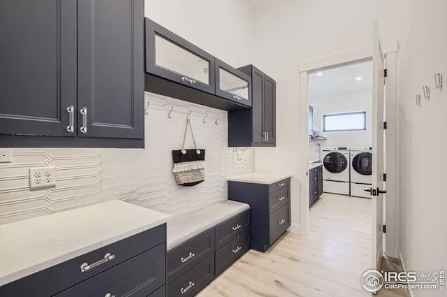 kitchen with washer and clothes dryer, backsplash, light countertops, light wood finished floors, and glass insert cabinets