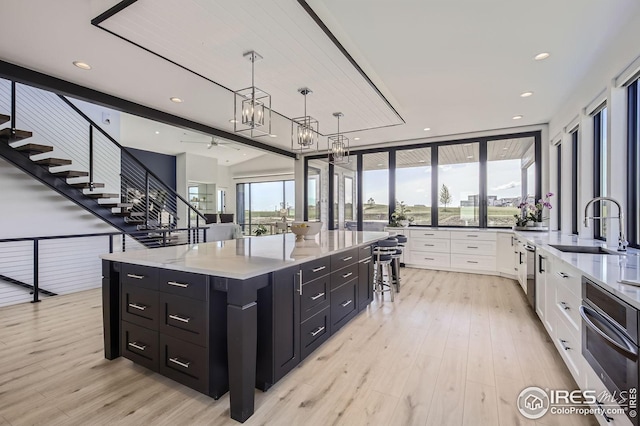 kitchen featuring dark cabinets, a sink, white cabinetry, and light wood finished floors
