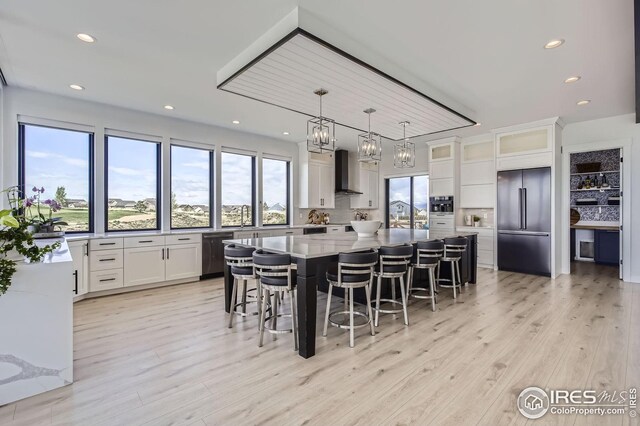 kitchen with stainless steel appliances, wall chimney range hood, white cabinetry, a kitchen bar, and a large island