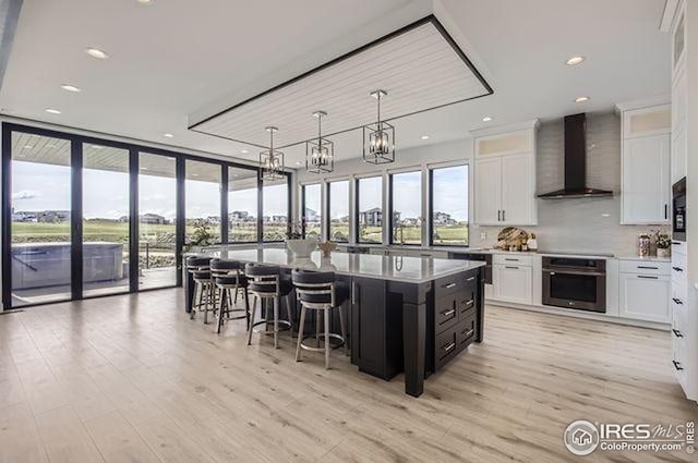 kitchen featuring wall chimney exhaust hood, stainless steel oven, white cabinetry, floor to ceiling windows, and recessed lighting