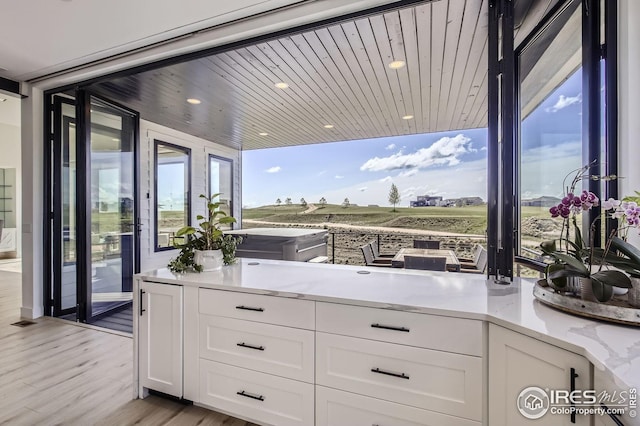 interior space featuring white cabinets, light wood finished floors, light stone counters, recessed lighting, and expansive windows