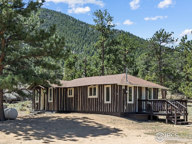 view of front of home with a forest view, dirt driveway, and a deck with mountain view