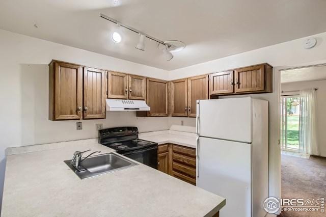 kitchen with freestanding refrigerator, black electric range oven, under cabinet range hood, a sink, and track lighting