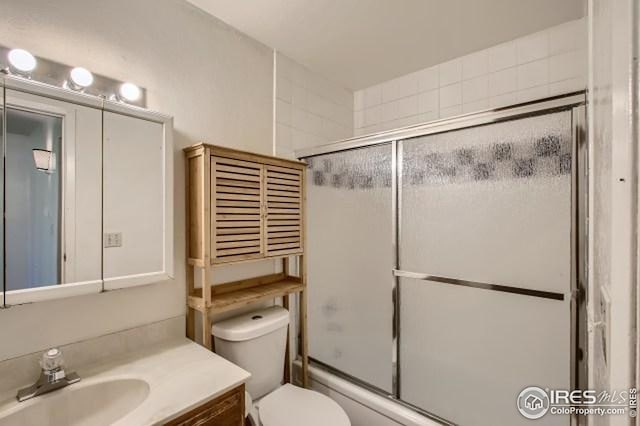 full bathroom with vanity, bath / shower combo with glass door, and toilet