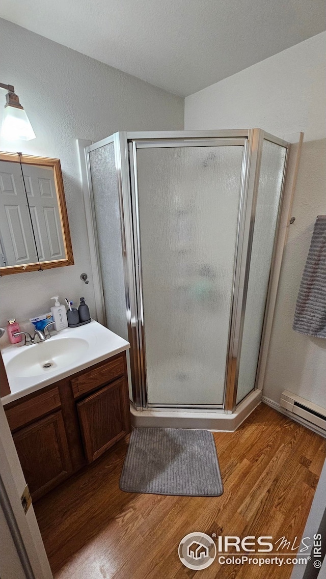 bathroom with wood finished floors, vanity, a stall shower, and a baseboard radiator