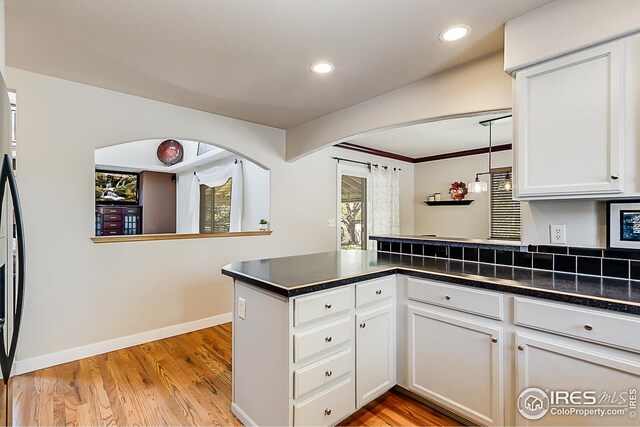 1108 Basin Ct, Windsor, CO 80550 - kitchen featuring a peninsula, arched walkways, dark countertops, light wood-style flooring, and white cabinets