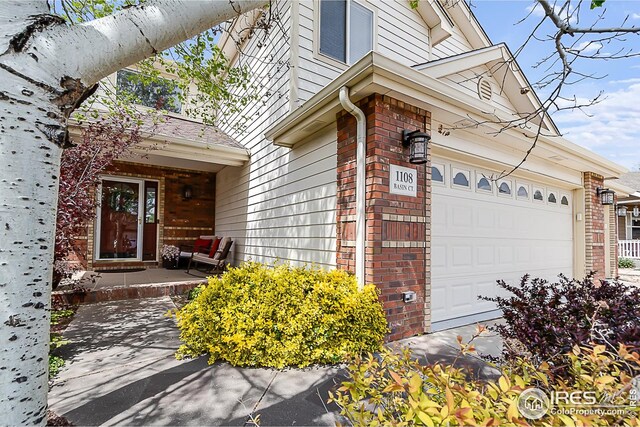 1108 Basin Ct, Windsor, CO 80550 - view of exterior entry featuring brick siding, a garage, and covered porch