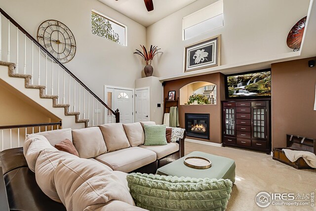 1108 Basin Ct, Windsor, CO 80550 - living area with carpet floors, a high ceiling, a glass covered fireplace, stairway, and a ceiling fan